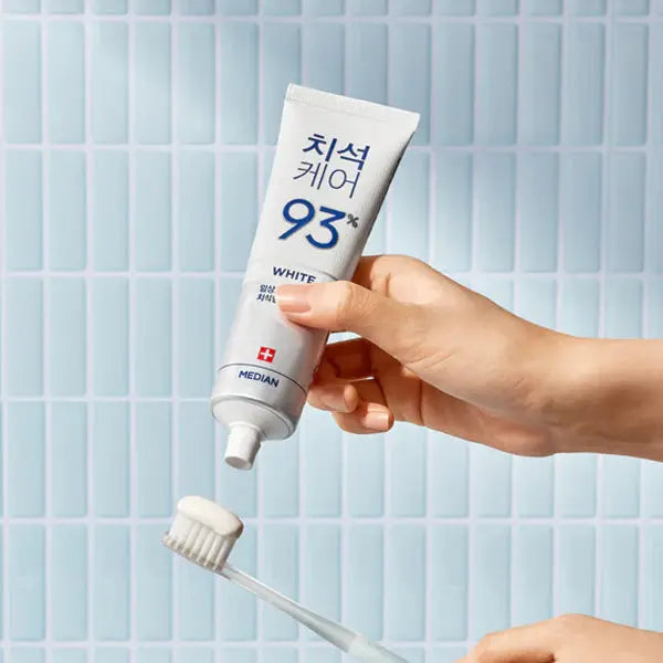Hand holding a tube of Median whitening toothpaste with a brush on a tiled bathroom background