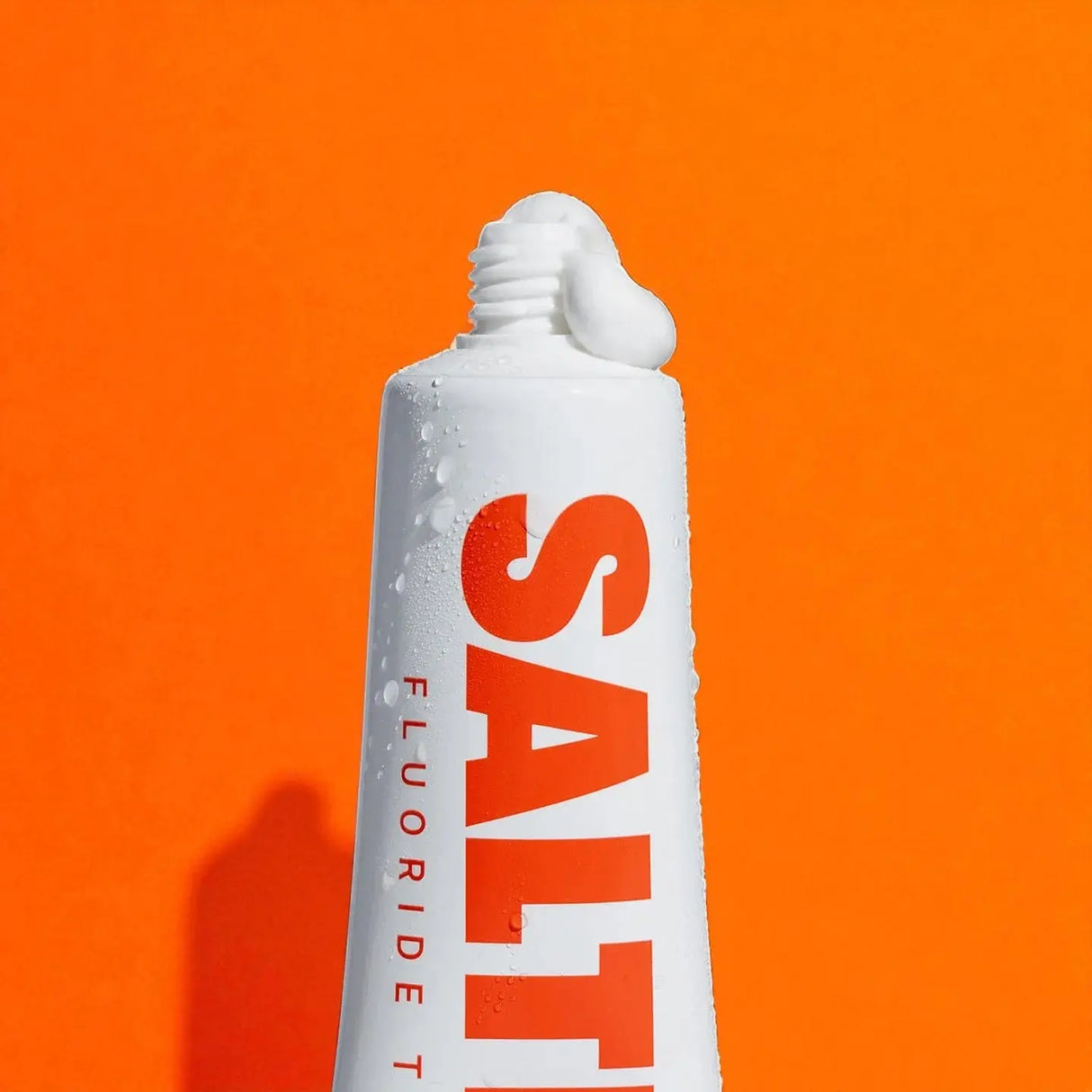 Saltrain fluoride toothpaste tube on an orange background