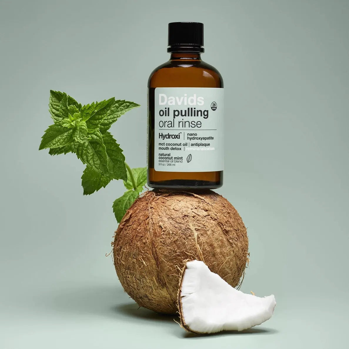 Bottle of Davids oil pulling oral rinse on a coconut with a green leaf on a light gray background