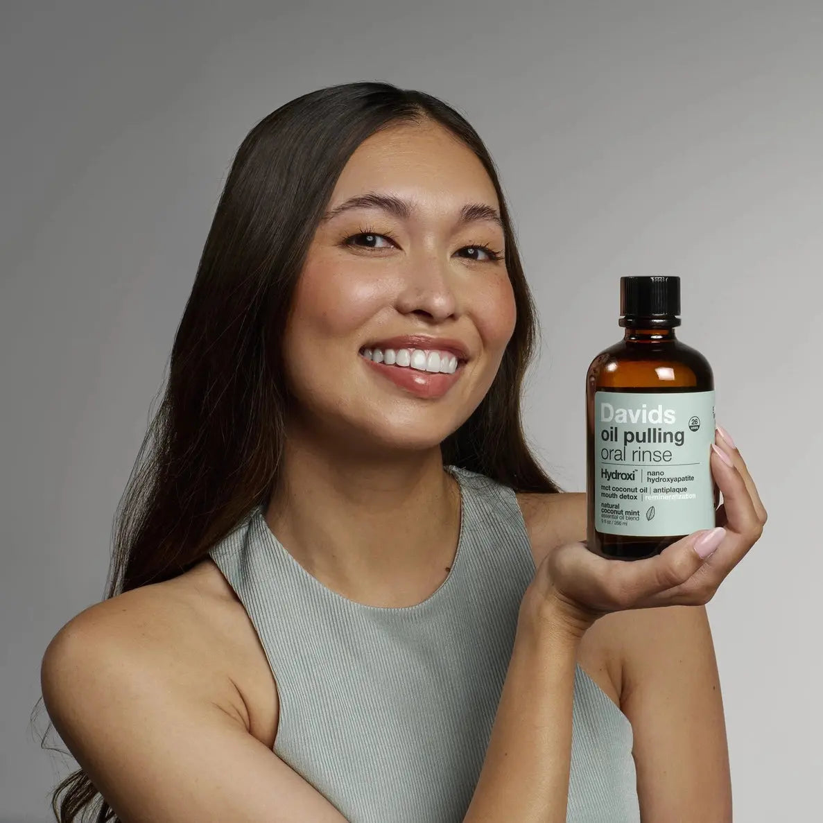 Woman holding a bottle of David's oil pulling oral rinse against a gray background