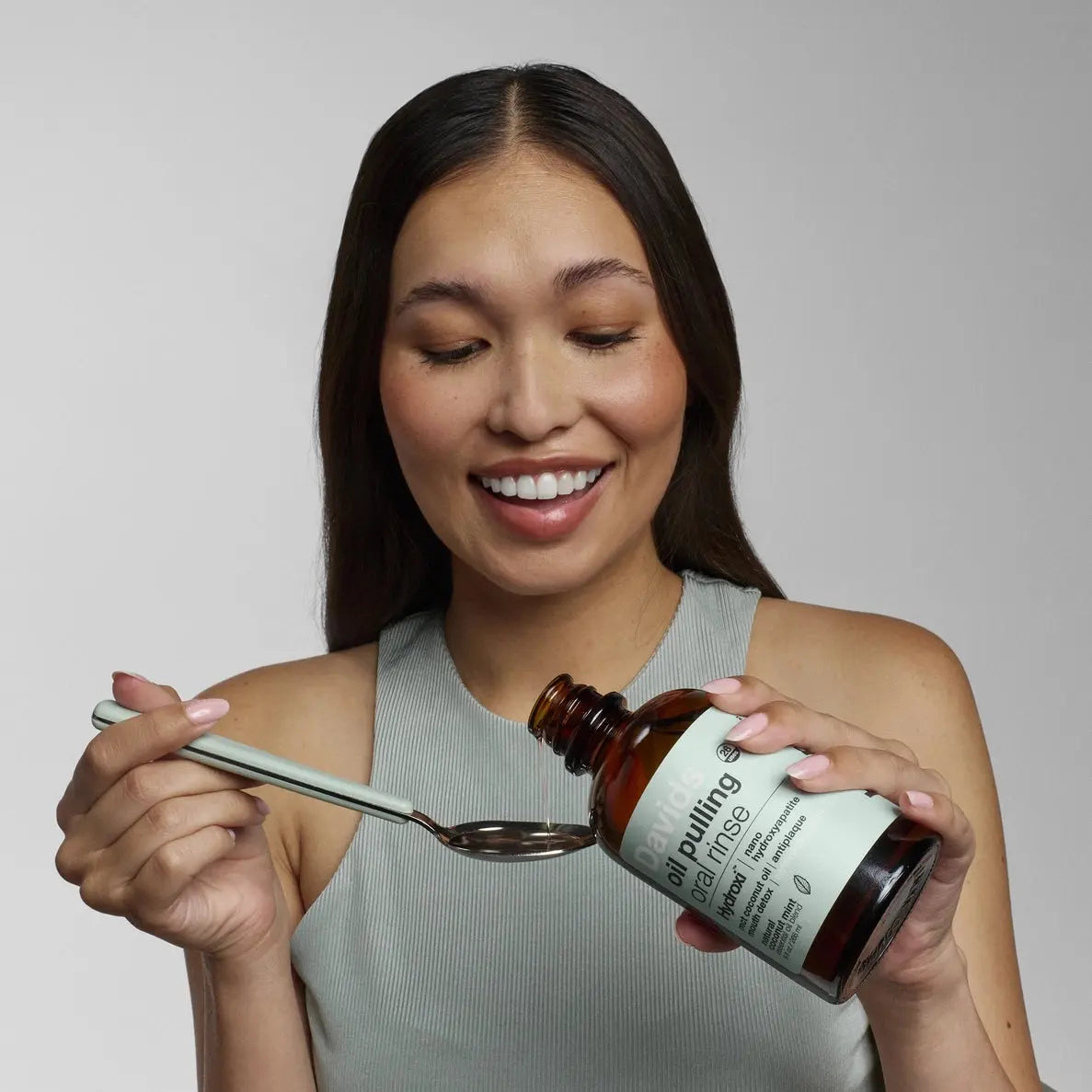 Woman pouring a bottle of Davids oil pulling rinse onto a spoon against a plain white background