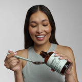 Woman pouring a bottle of Davids oil pulling rinse onto a spoon against a plain white background