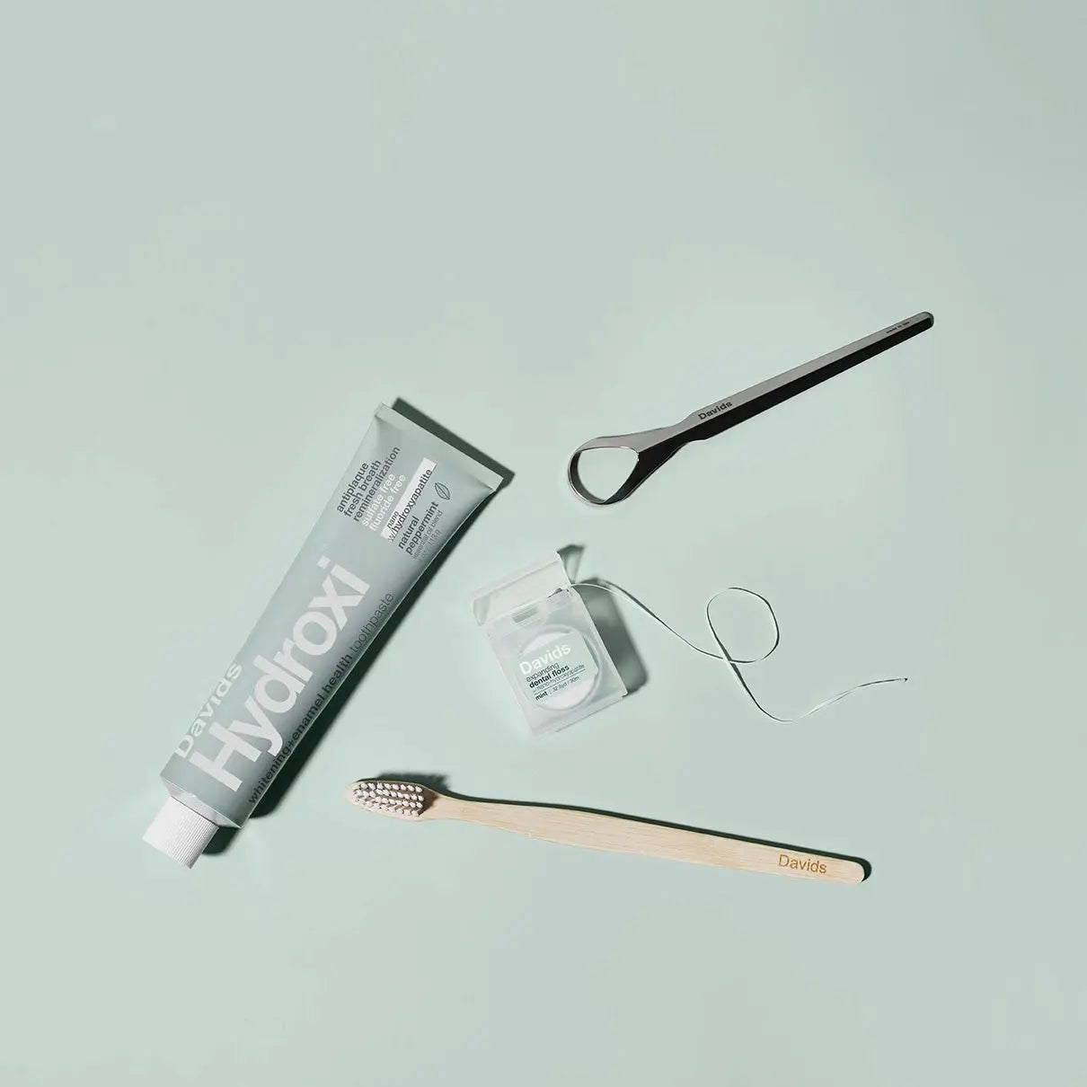 Hydroxi toothpaste tube, wooden toothbrush, and dental floss on a light blue background