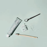 Hydroxi toothpaste tube, wooden toothbrush, and dental floss on a light blue background