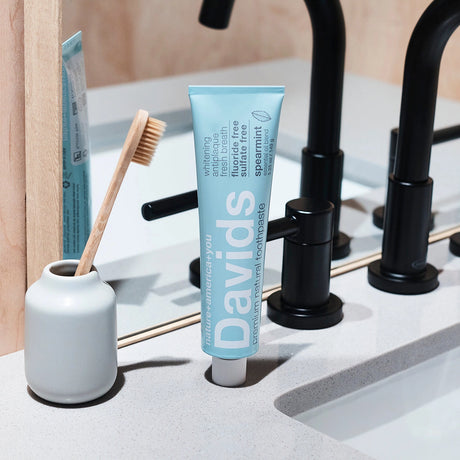 Tube of Davids toothpaste on a bathroom counter with a toothbrush and container.