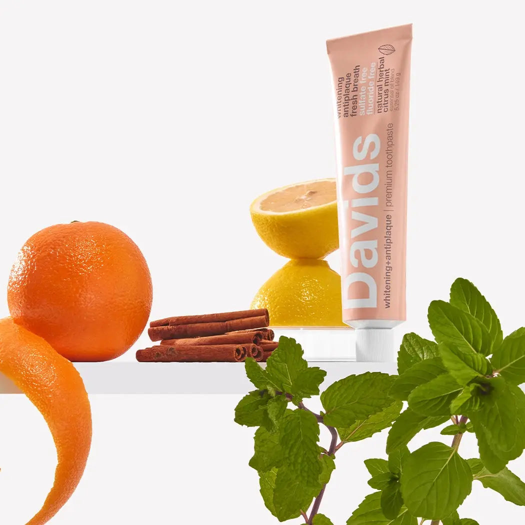 Davids toothpaste tube with oranges, lemons, cinnamon sticks, and mint leaves on a white background