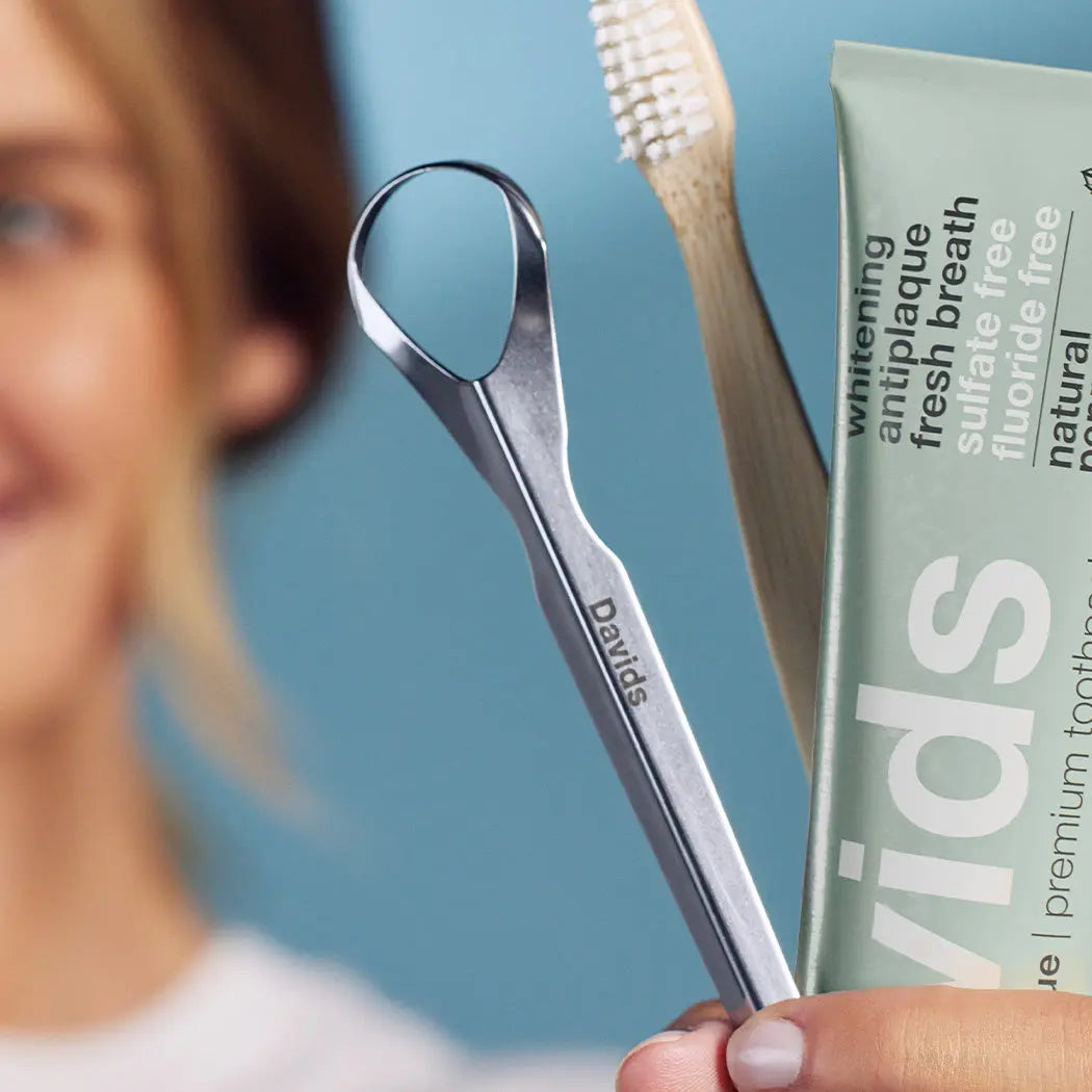 person holding a davids professional tongue scraper with a davids toothpaste and toothbrush