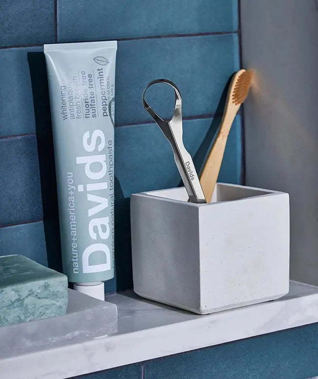 Bathroom shelf with Davids toothpaste, soap, and toungue scraper against a blue tiled wall.