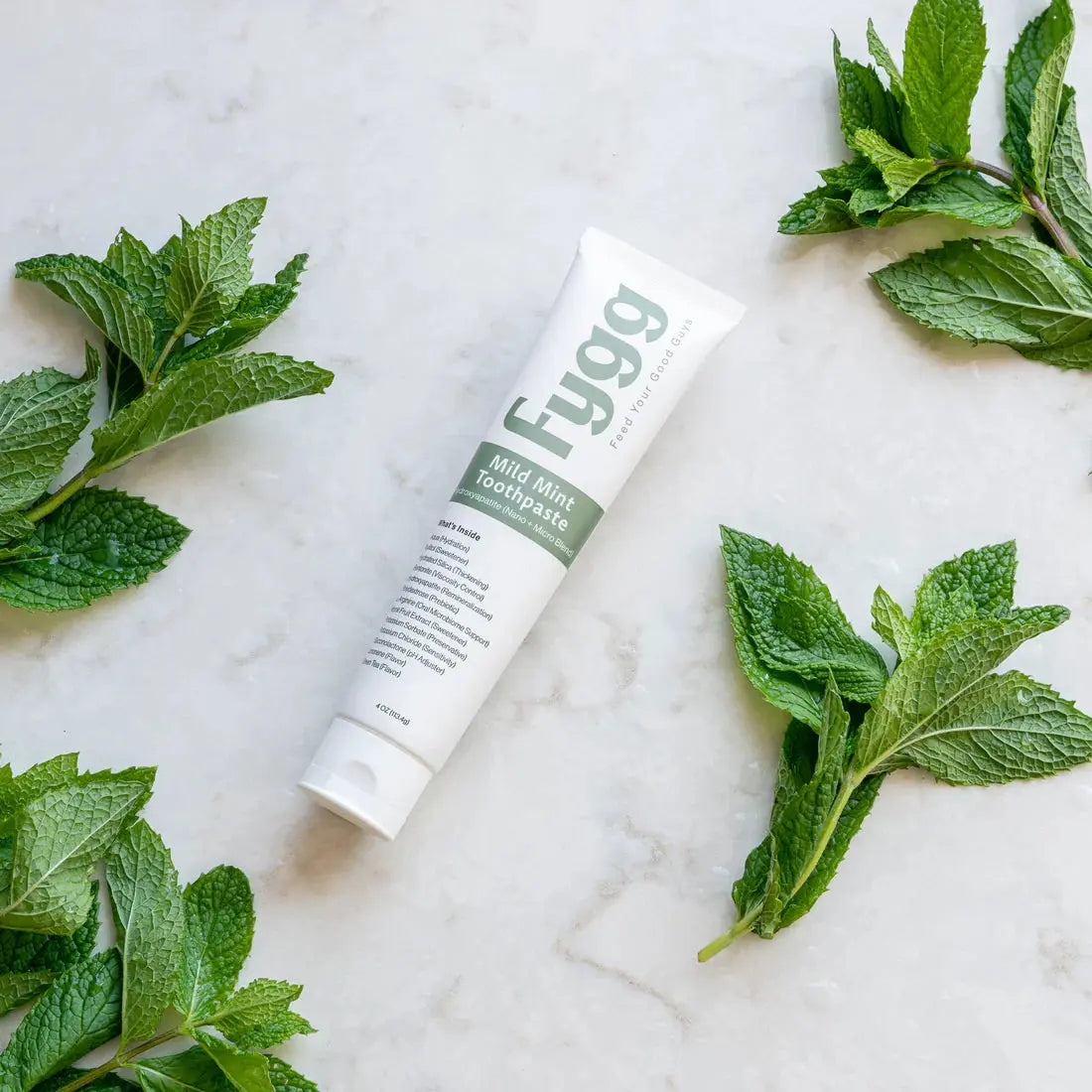 Fygg toothpaste tube surrounded by mint leaves on a marble surface