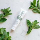 Fygg toothpaste tube surrounded by mint leaves on a marble surface