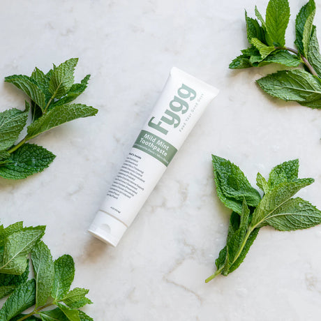 Fygg toothpaste tube surrounded by mint leaves on a marble surface