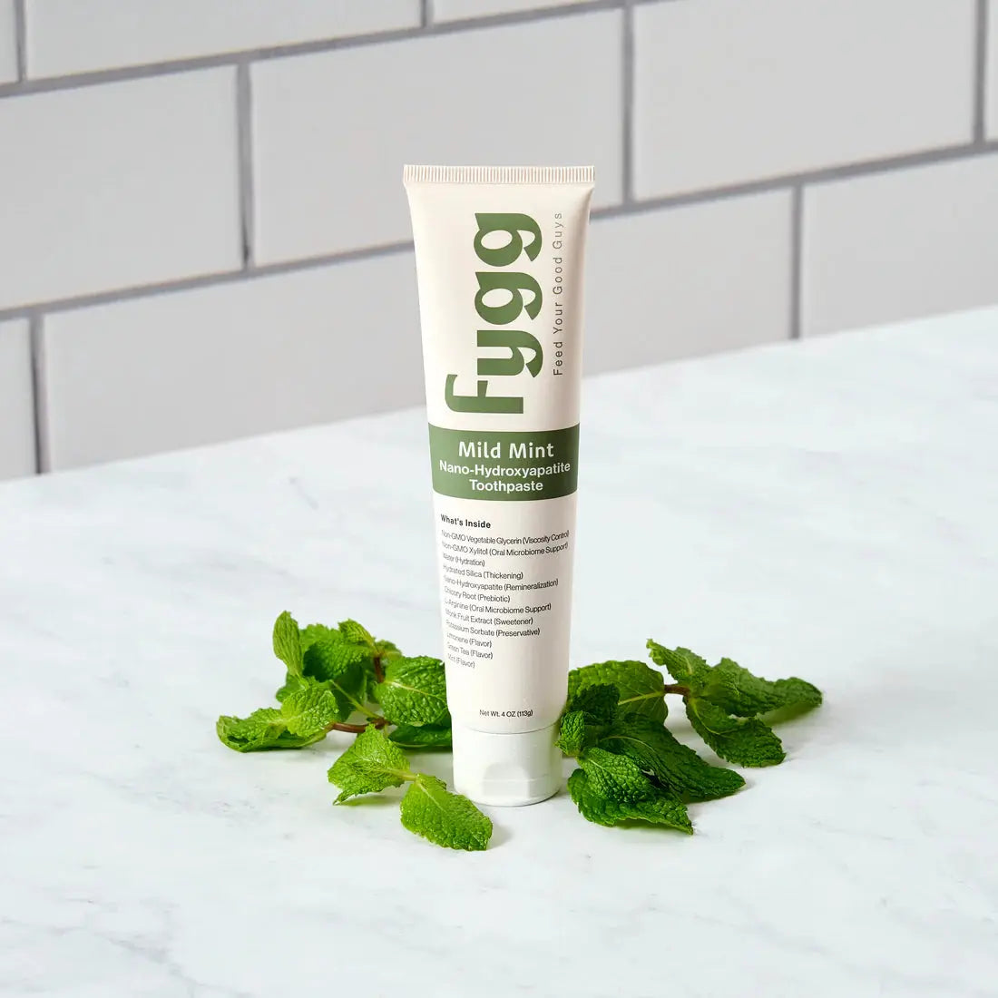Fygg toothpaste tube with fresh mint leaves on a white surface
