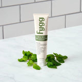 Fygg toothpaste tube with fresh mint leaves on a white surface